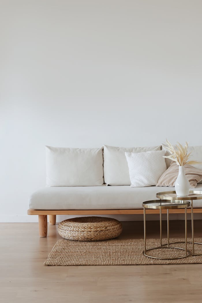 Mastering the First Impression: Your intriguing post title goes here A chic minimalist living room featuring a white sofa with cushions, dried flowers in a vase, and a wooden floor.